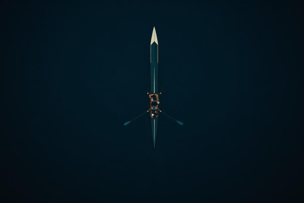 Aerial view of a rowing crew in synchronised stroke on dark water